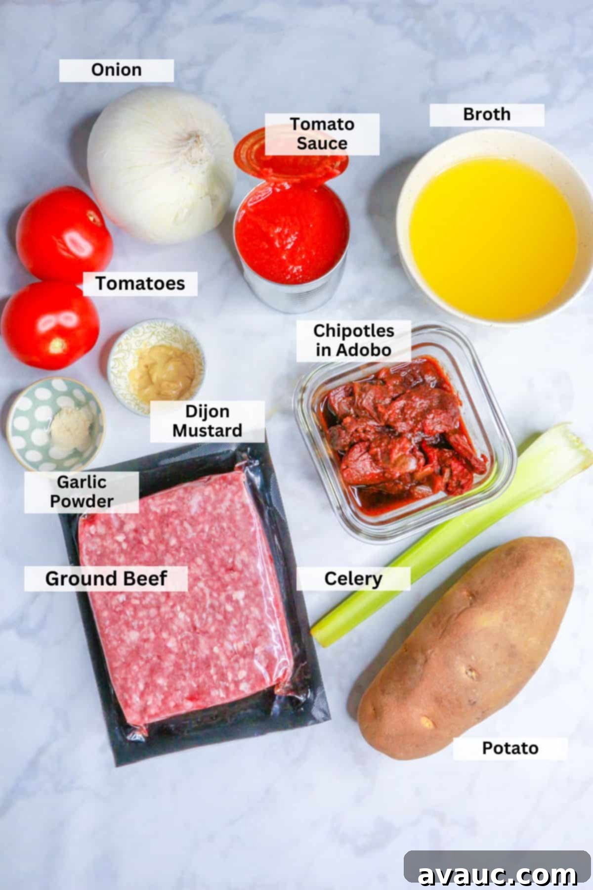 Ingredients for albondigas in chipotle sauce: onion, tomatoes, tomato sauce, broth, chipotles, celery, potato, dijon mustard, garlic powder, ground beef laid out on a white surface.