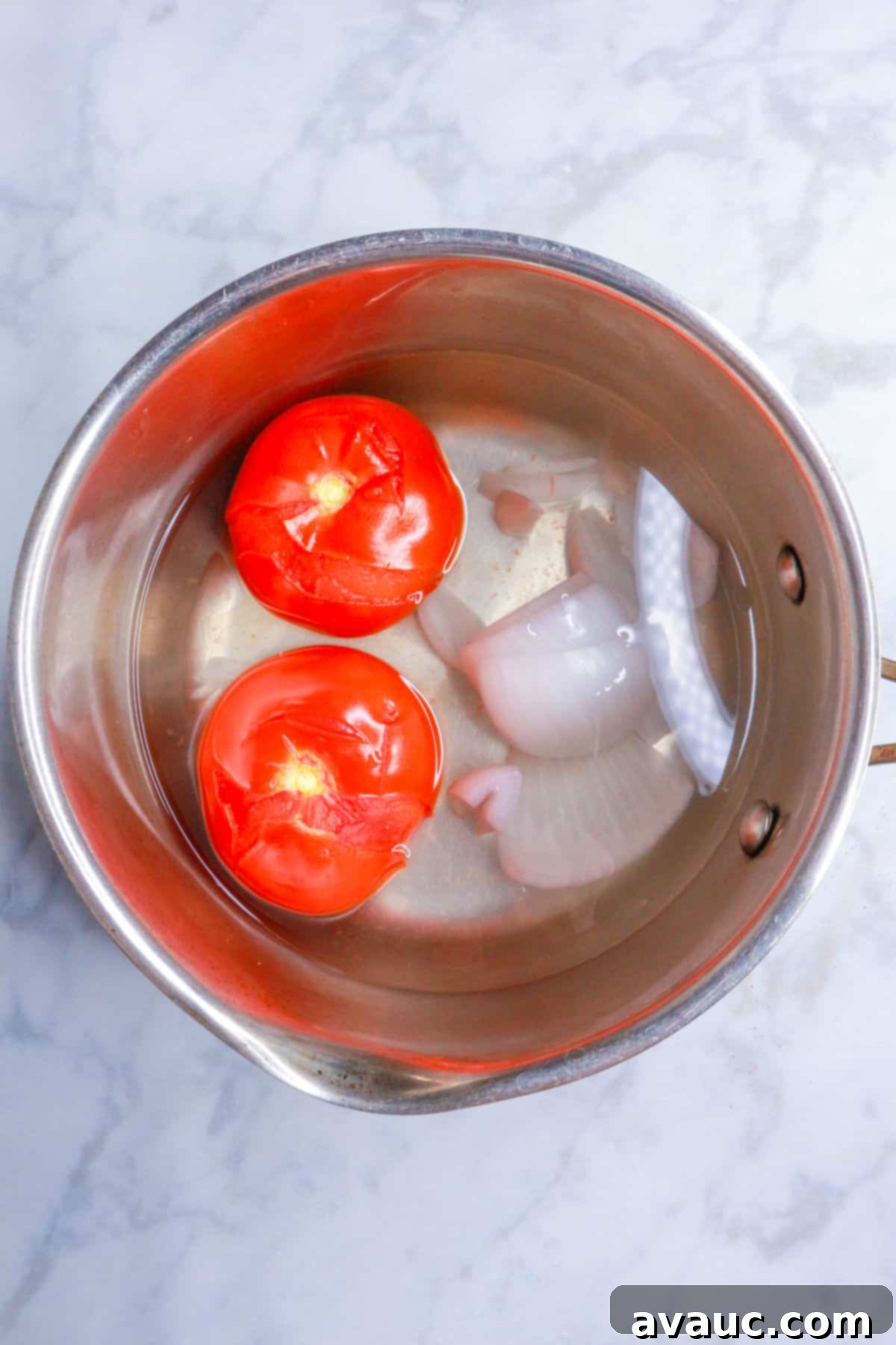 Small pot with boiled Roma tomatoes and a piece of white onion, ready to be blended for the sauce.