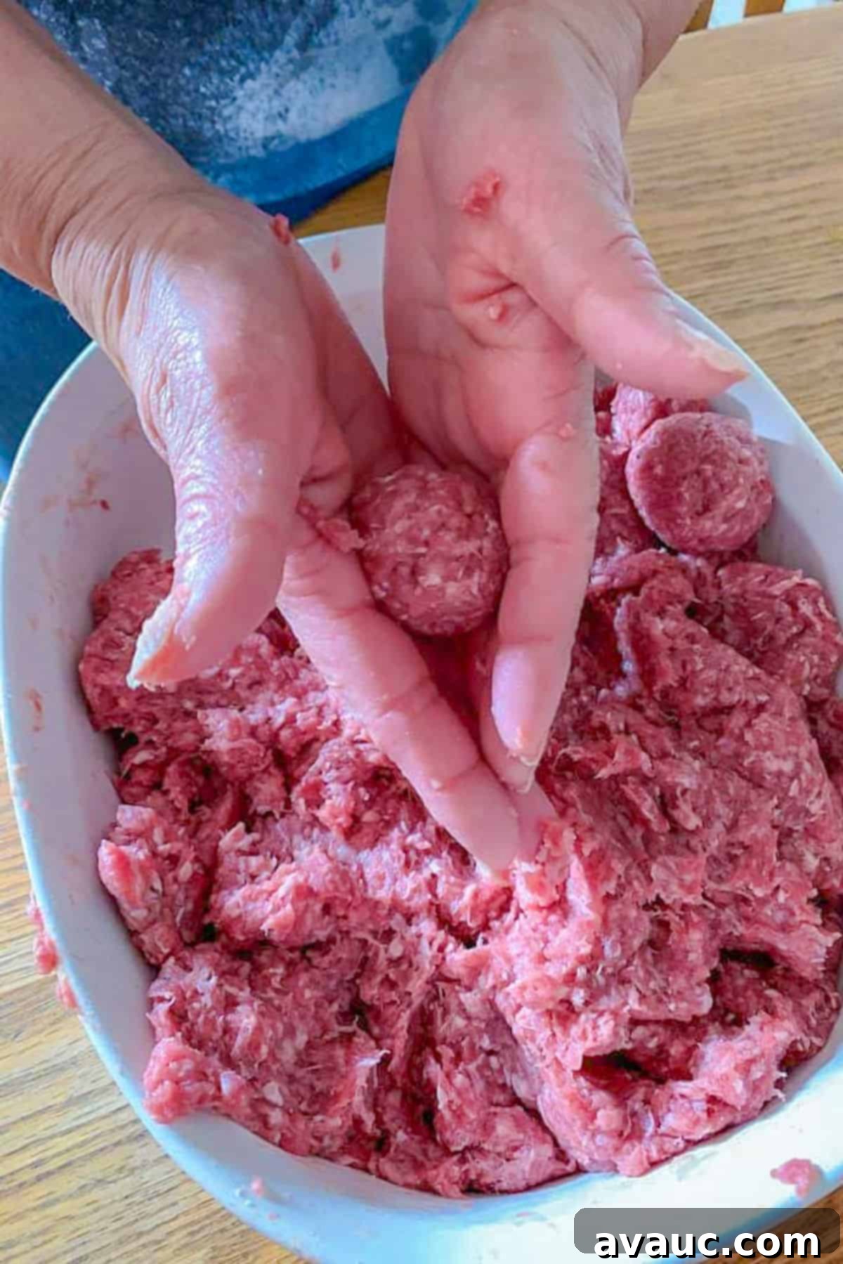 Bowl of raw seasoned ground beef with hands forming uniform 1-inch meatballs.
