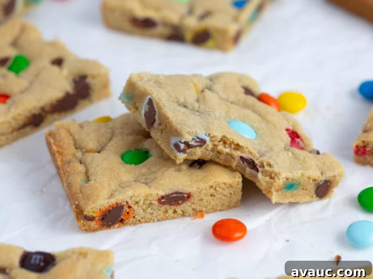 Close-up of a single chewy M&M Cookie bar square with a bite taken out, revealing its soft interior and melted chocolate.