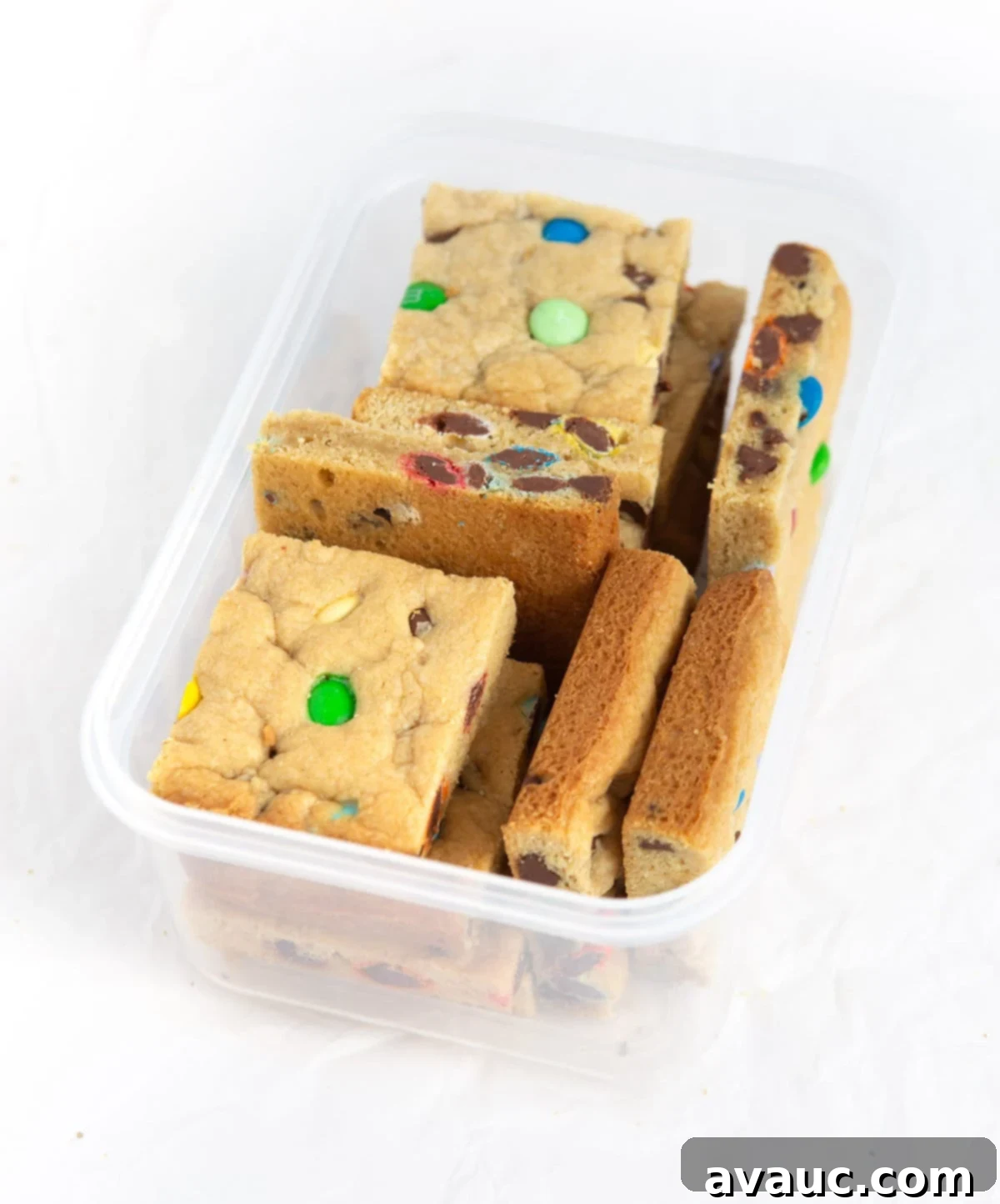 Colorful Chewy M and M Cookie Bars 9 Cut M&M cookie bars neatly stacked in a plastic container, ready for freezing or storage.