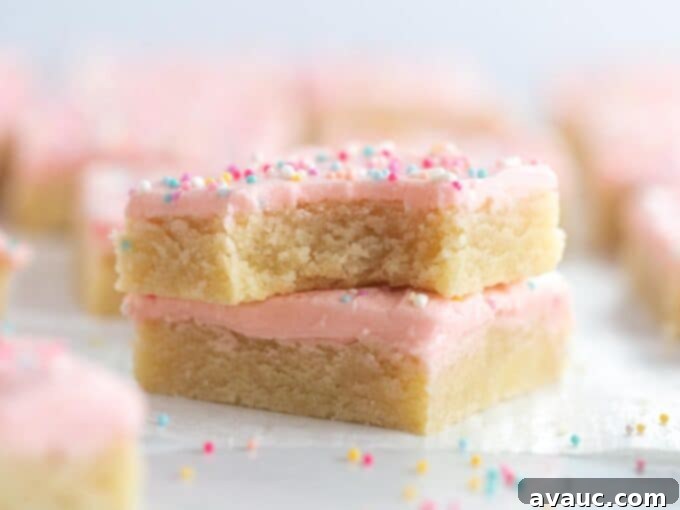 Soft frosted sugar cookie bars with a bite taken out, showing the tender crumb