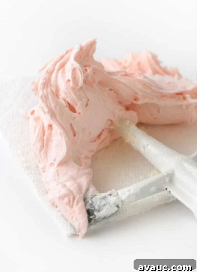Pink buttercream frosting on a KitchenAid paddle attachment, showing its creamy texture