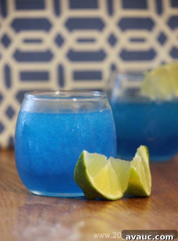 Easy Homemade Blue Slushies 1 Refreshing Blue Raspberry Slushie in a tall glass, garnished with lime slices, perfect for summer.
