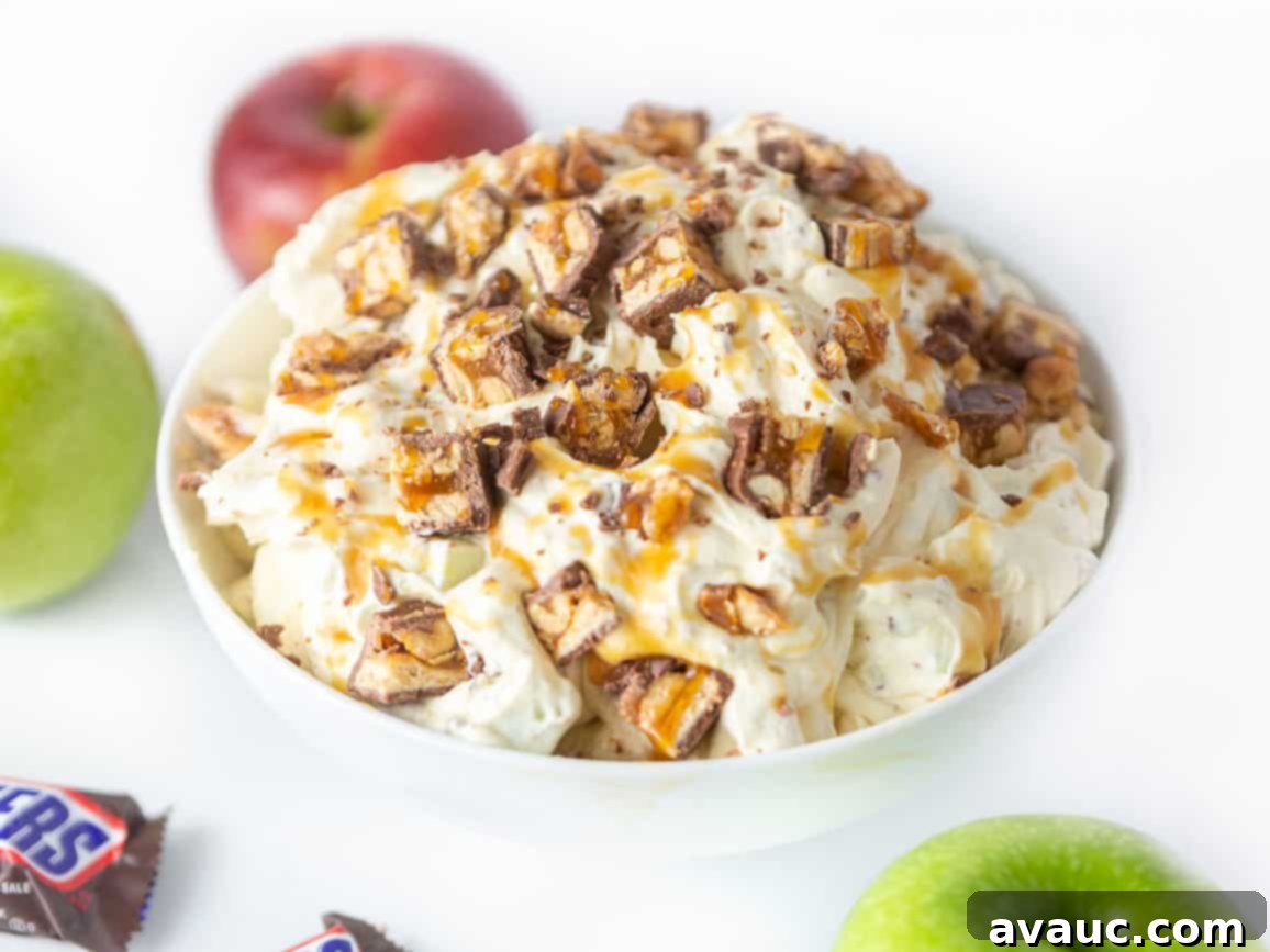 Bowl of creamy apple snickers salad dessert, topped with chopped snickers candy bars, apples, and caramel sauce