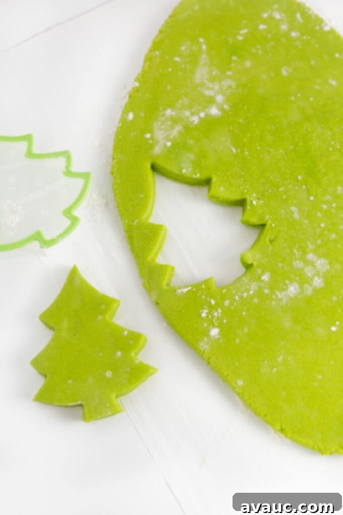 Effortless Christmas Tree Cookies 7 Green sugar cookie dough with multiple Christmas tree shapes already cut out and positioned, ready for decoration, against a light background.