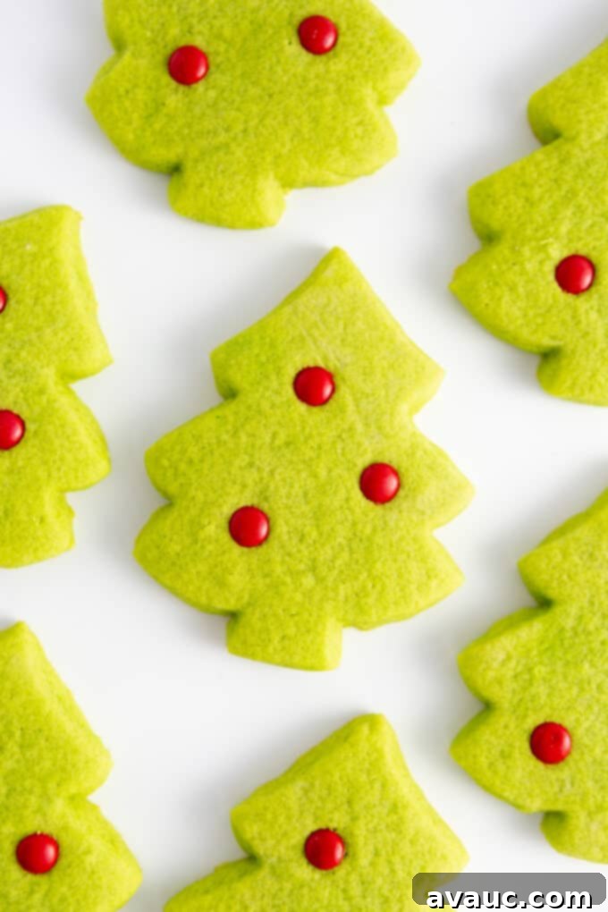 Effortless Christmas Tree Cookies 9 A single perfectly baked green Christmas tree sugar cookie, decorated with shiny red M&M ornaments, presented against a soft-focus background.