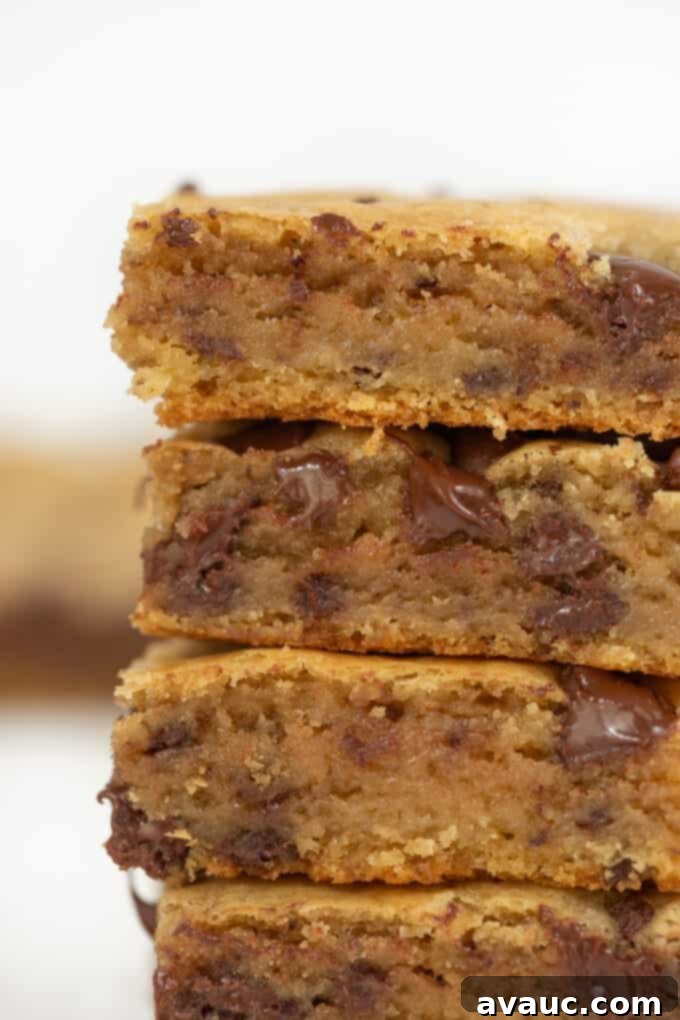 Irresistible Chocolate Chip Squares 4 A stack of chocolate chip cookie bars on a white plate, with a few chocolate chips scattered around.