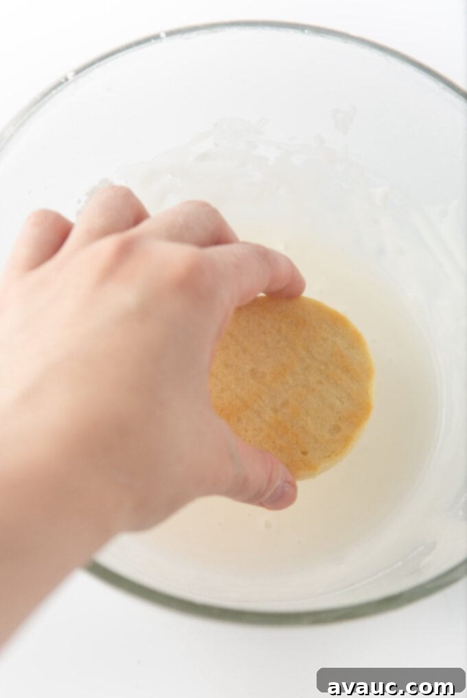 Quick and Easy Snowman Cookies 5 a hand carefully dipping the top of a sugar cookie into a bowl of smooth white icing