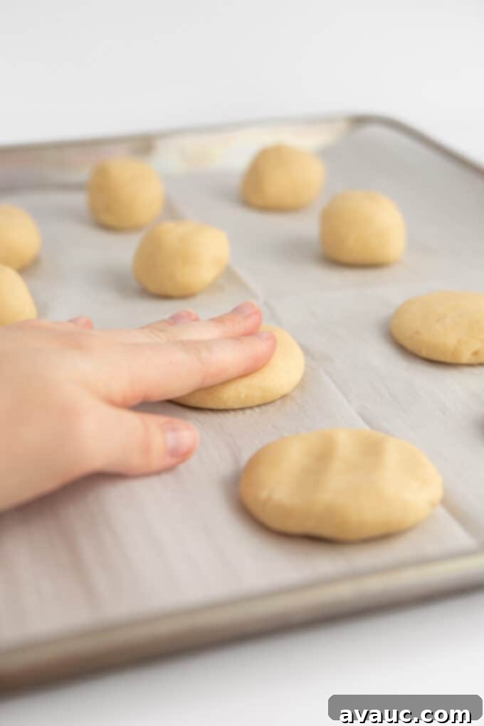 Hand pressing a scooped ball of fluffy sugar cookie dough to flatten it before baking