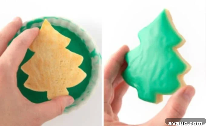 Simple Ways to Decorate Christmas Tree Cookies 7 A hand carefully dipping a cooled Christmas tree shaped sugar cookie into a bowl of smooth, green icing glaze, showcasing the simple and effective dipping technique