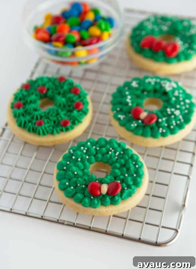 Green buttercream wreath sugar cookies, decorated with red M&Ms as bows, on a metal cooling rack