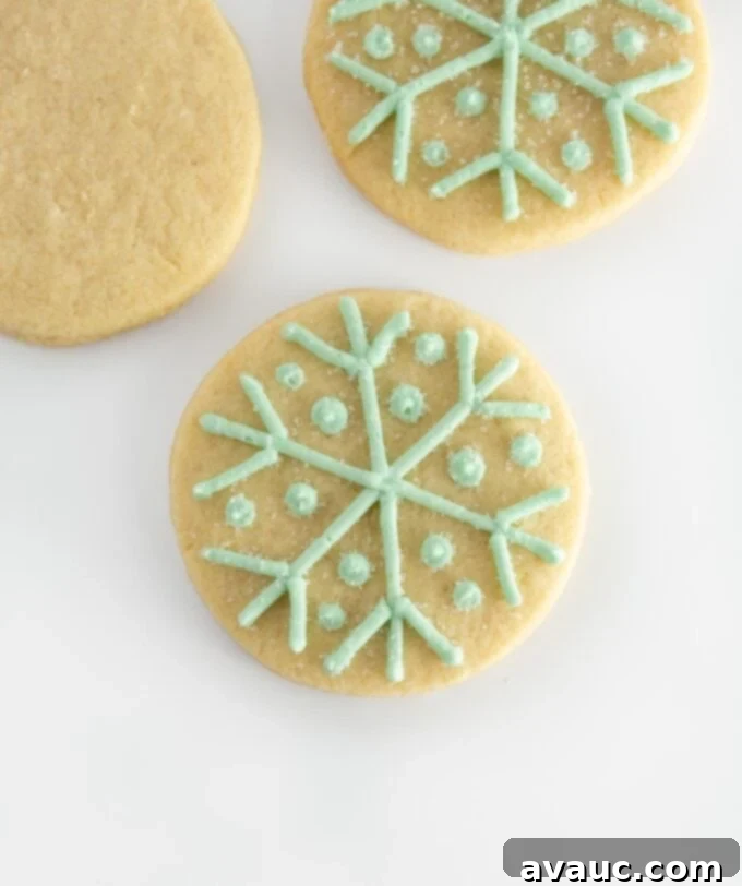 5 Easy Winter Cookie Recipes 8 A beautifully decorated round snowflake cookie with piped white frosting lines and dots, sprinkled with sanding sugar, on a pale blue background.