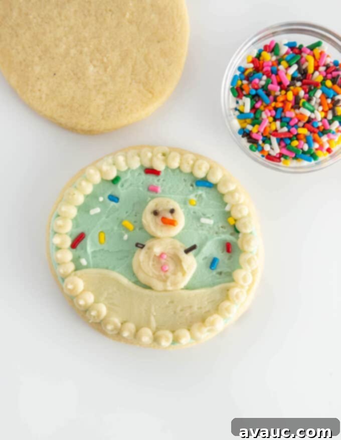 5 Easy Winter Cookie Recipes 9 A whimsical round snow globe cookie featuring a white snowman made of piped circles and sprinkle details on a pale blue background with white snowy ground.