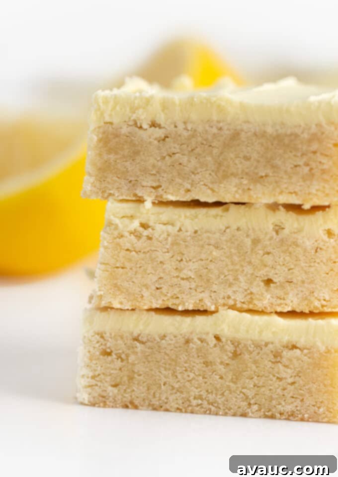 A tantalizing stack of lemon sugar cookie bars, generously frosted with vibrant lemon buttercream, showcasing their delightful golden hue.