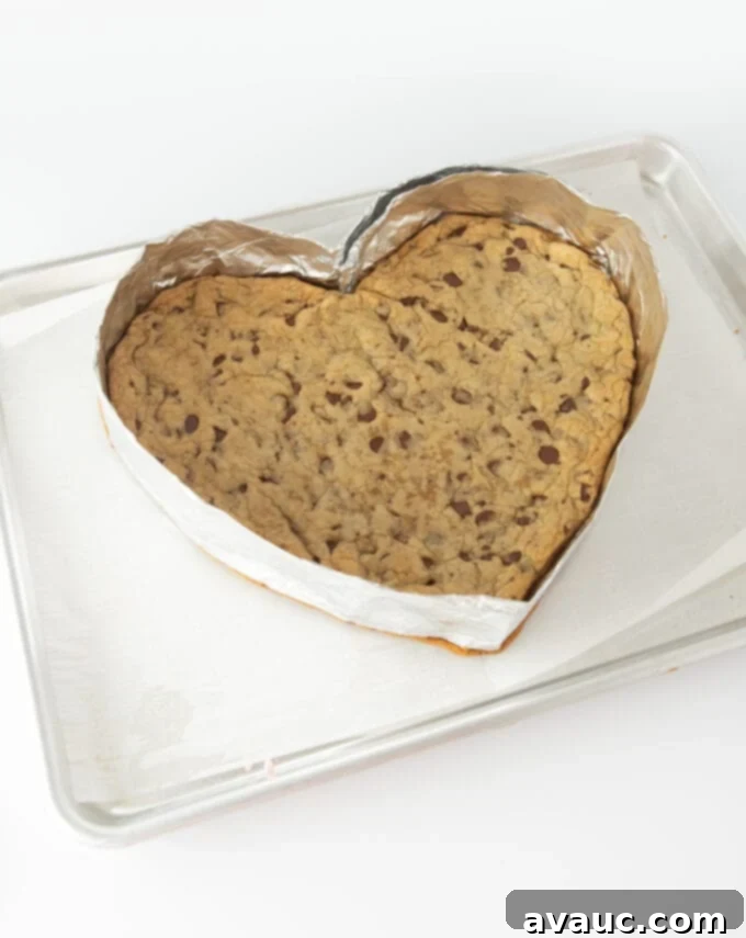 Freshly baked heart-shaped cookie cake cooling on parchment paper with foil removed