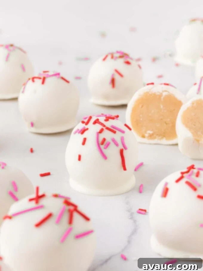 Valentines Day Sugar Cookie Truffles 6 A close-up shot of several sugar cookie Valentine truffles on a cooling rack, showcasing their pristine white chocolate coating and vibrant red and pink sprinkles.