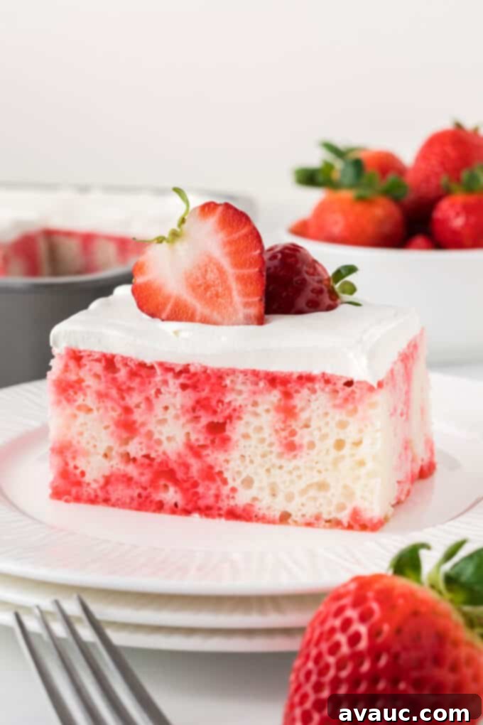 Strawberry Burst Poke Cake 9 Strawberry jello poke cake with whipped cream frosting on white plate, garnished with strawberries