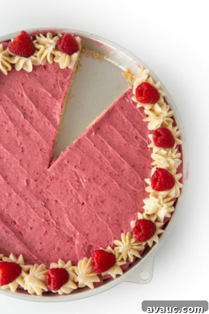 Decadent White Chocolate Raspberry Cookie Cake 2 A stunning slice of white chocolate raspberry cookie cake on a white plate, showcasing its soft texture and generous frosting, with fresh raspberries on top.