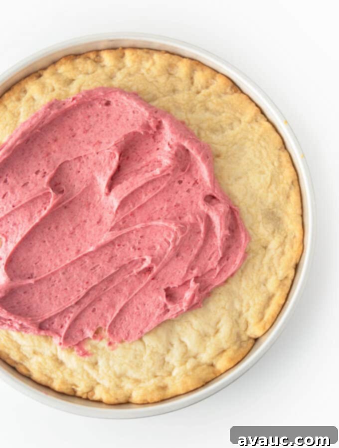 Decadent White Chocolate Raspberry Cookie Cake 4 A freshly baked white chocolate raspberry cookie cake, still in its round pan, cooling on a wire rack.