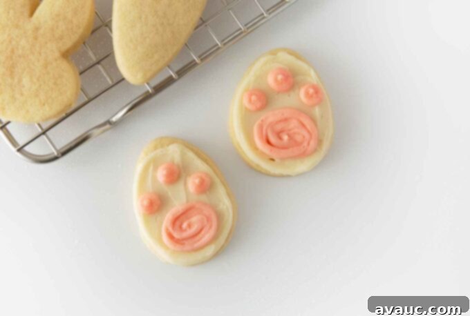7 Delightful Easter Cookie Designs, Made Easy 12 Easter egg shaped sugar cookie decorated with white frosting and three pink dots to look like bunny paw