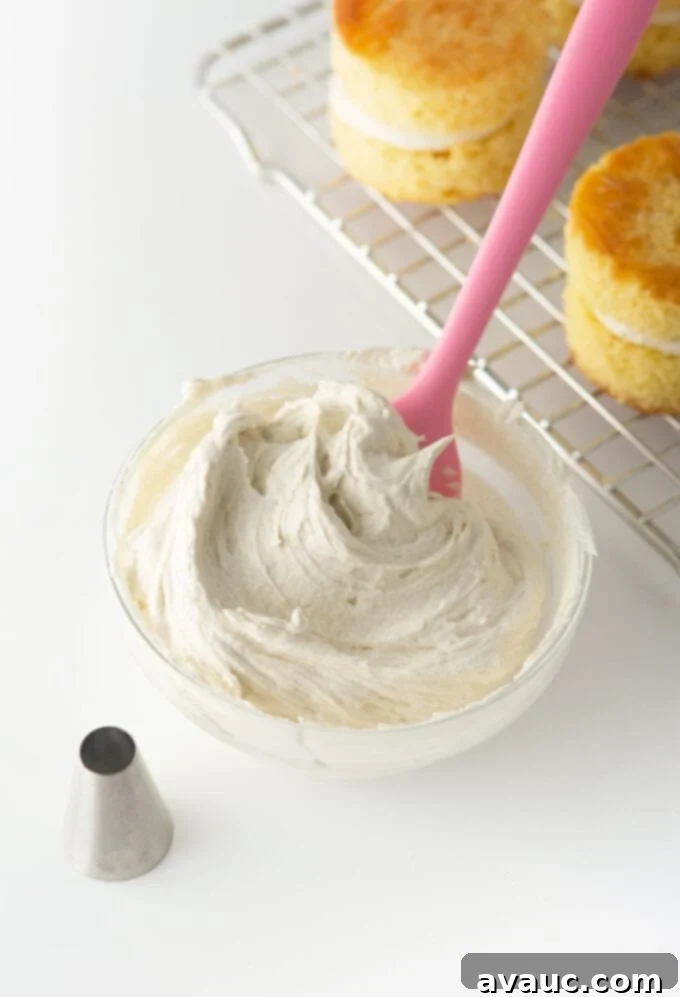 Close-up of fluffy white buttercream frosting being piped into a clear piping bag with a large round tip, preparing for cake assembly.