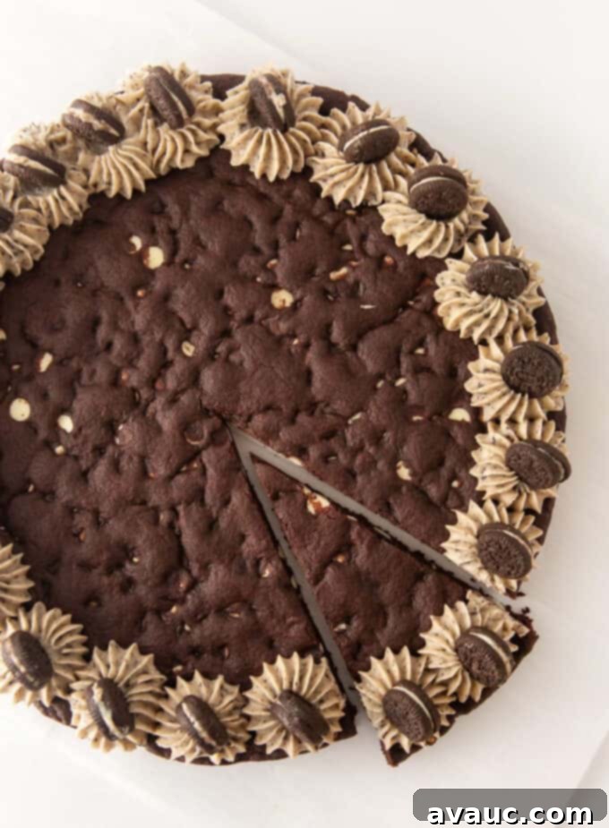Oreo Dream Cake 2 Overhead view of decorated Oreo pizza cookie cake with one slice cut, showcasing its soft and chewy texture.