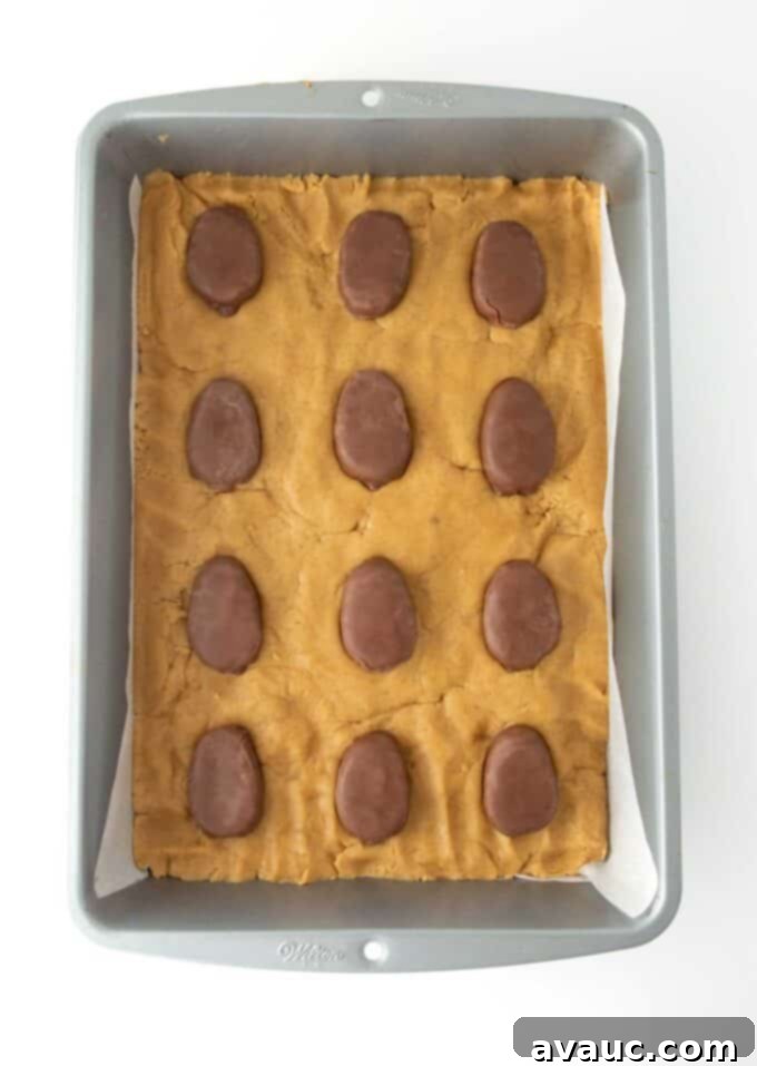 Reese's Egg Bliss Bars 5 Peanut butter cookie dough pressed into a metal 9x13 pan and topped with 12 Reese's eggs, ready for baking.