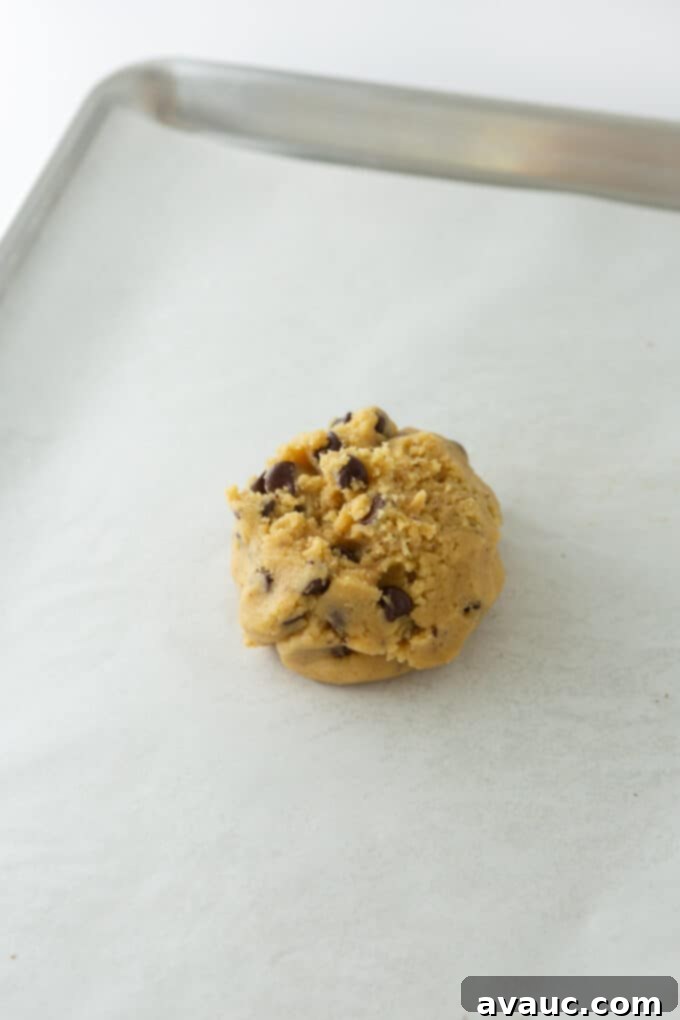One Epic Chocolate Chip Cookie 7 Raw giant chocolate chip cookie dough ball on a parchment-lined baking sheet.