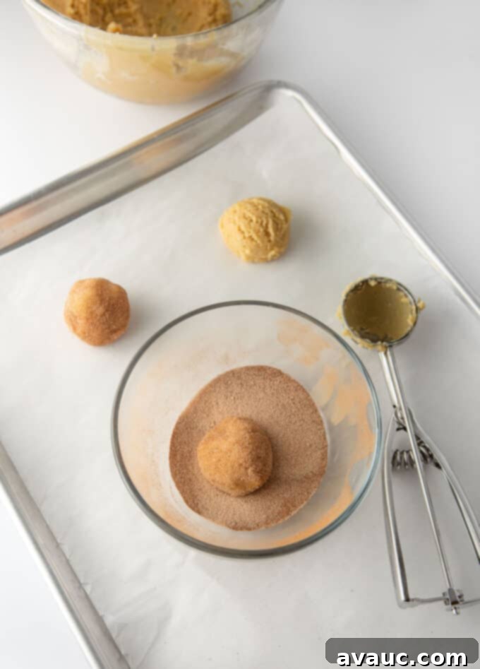 Metal baking pan with scoops of cookie dough and bowl of cinnamon sugar to roll cookies in