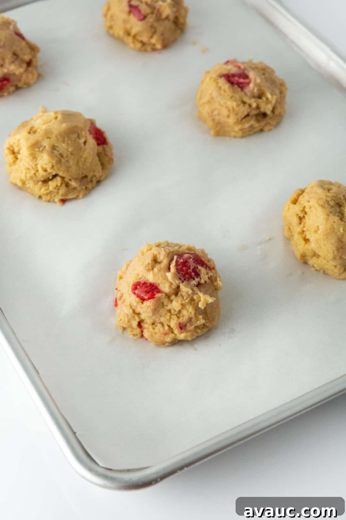 Cheesecake Filled Strawberry Cookies 7 Two silver trays show cookie dough balls being wrapped around cheesecake filling and filled with strawberries, ready for baking.