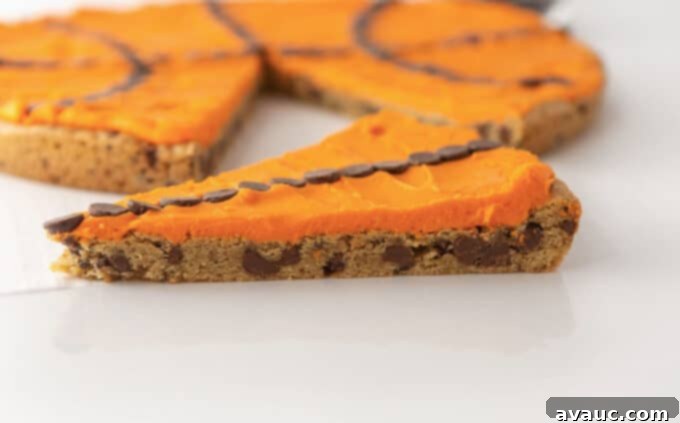 Slice of chocolate chip cookie cake decorated with orange frosting and chocolate chips, showing its soft and chewy interior