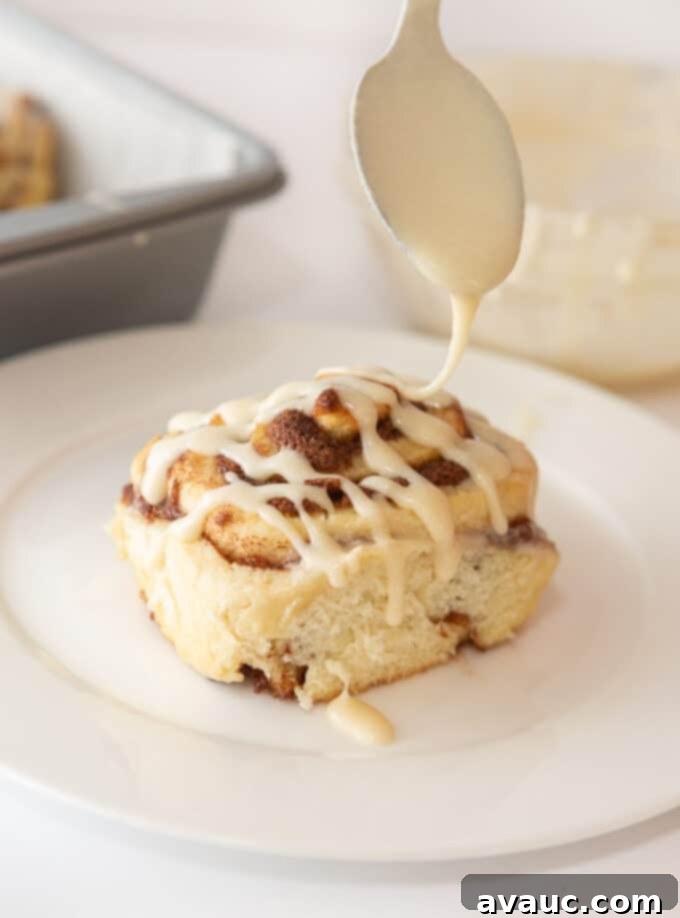 Drizzly cinnamon roll icing on freshly baked cinnamon rolls, showcasing its smooth, pourable texture.