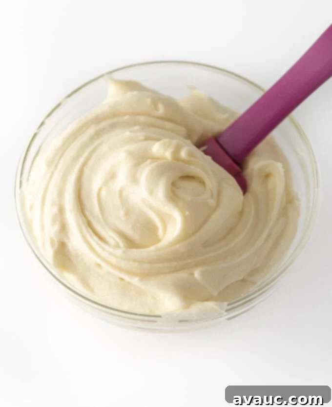 Close-up of fluffy cream cheese frosting in a bowl with a spoon.