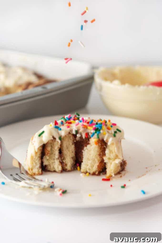 A tray of freshly baked cinnamon rolls being generously frosted with cream cheese icing.