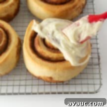 A round dish of cinnamon rolls covered in cream cheese frosting, with one roll taken out.