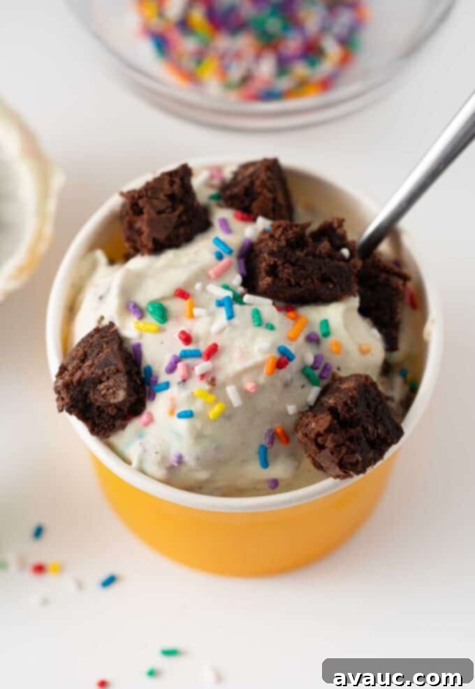 Cup of cake batter ice cream topped with brownie bites and colorful sprinkles, ready to be served.