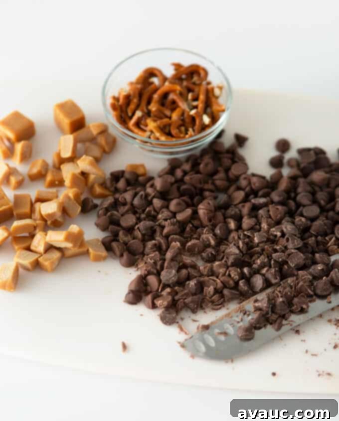Chopped chocolate chips, caramel pieces, and broken pretzels ready to be added to cookie dough.