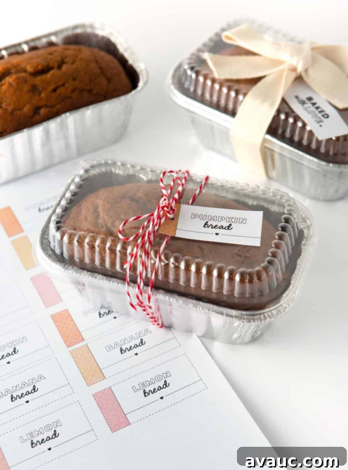 A charmingly packaged mini pumpkin bread loaf nestled in a disposable foil pan, elegantly tied with red string and adorned with a festive gift tag, showcasing a perfect presentation for sharing.