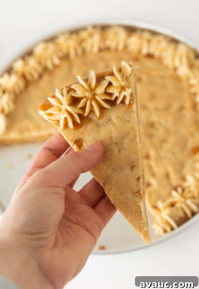 Decadent Chewy Butterscotch Chip Cookie Cake 3 Hand holding a perfectly sliced piece of butterscotch cookie cake, showing its thick, soft center and frosted edge.