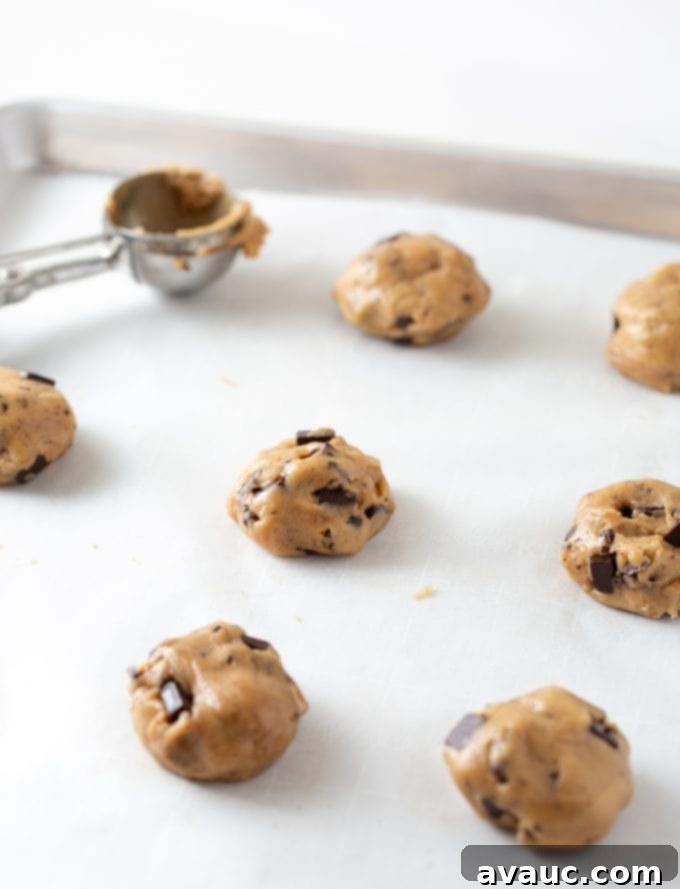 One Bowl Chocolate Chip Bliss 8 Chocolate chip cookie dough scoops, flattened into discs, arranged on a baking tray lined with parchment paper.