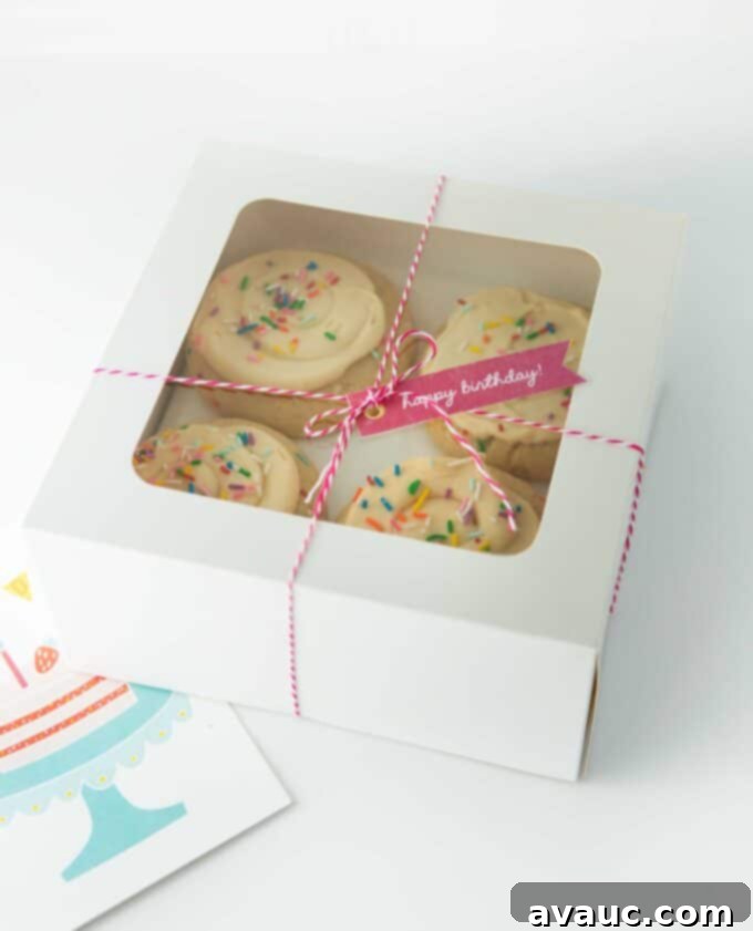 A beautiful square white bakery box featuring a clear window, elegantly displaying an assortment of perfectly frosted sugar cookies, ready for a special gift.