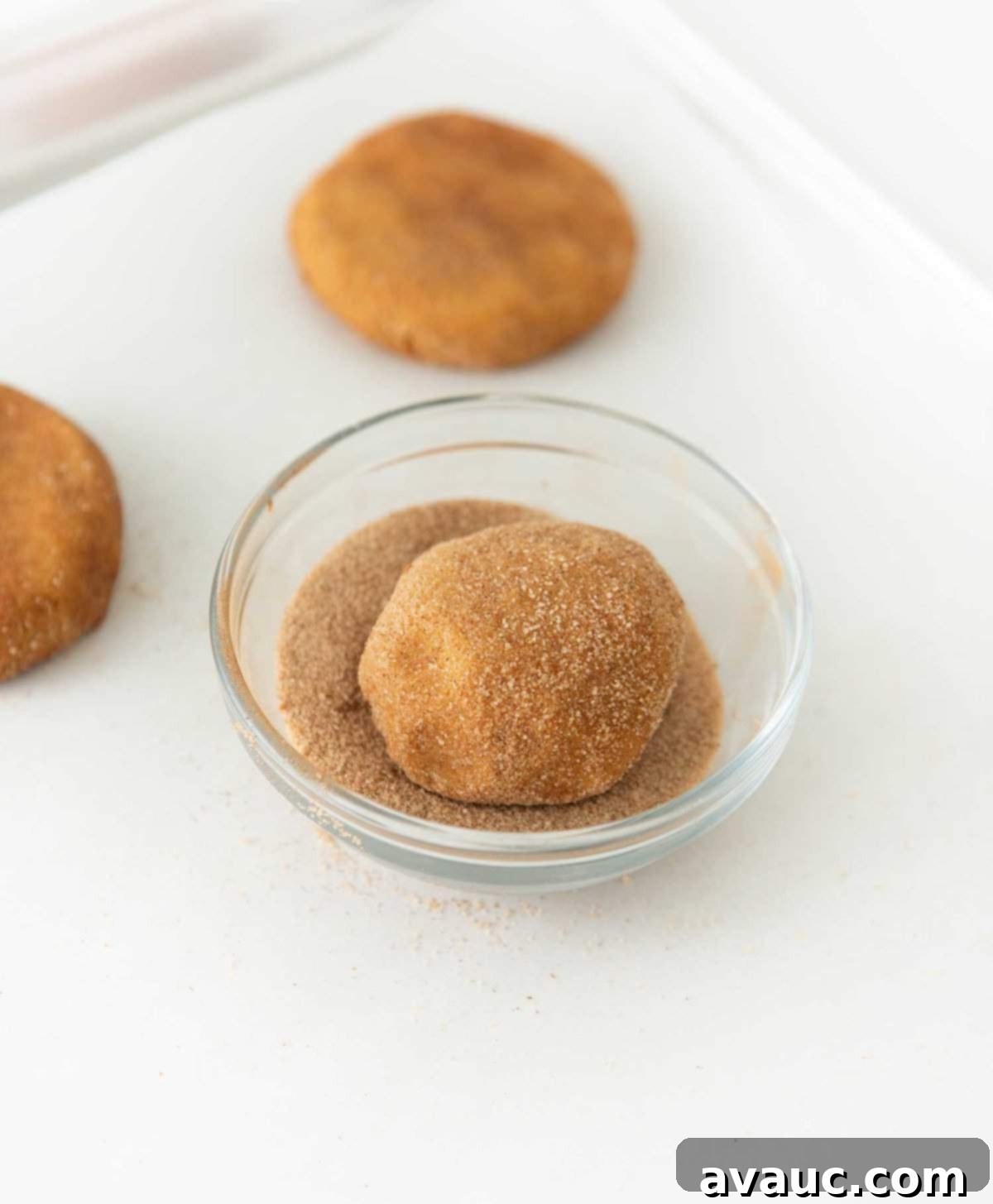 Rolling pumpkin snickerdoodle dough balls in a bowl of cinnamon sugar mixture.