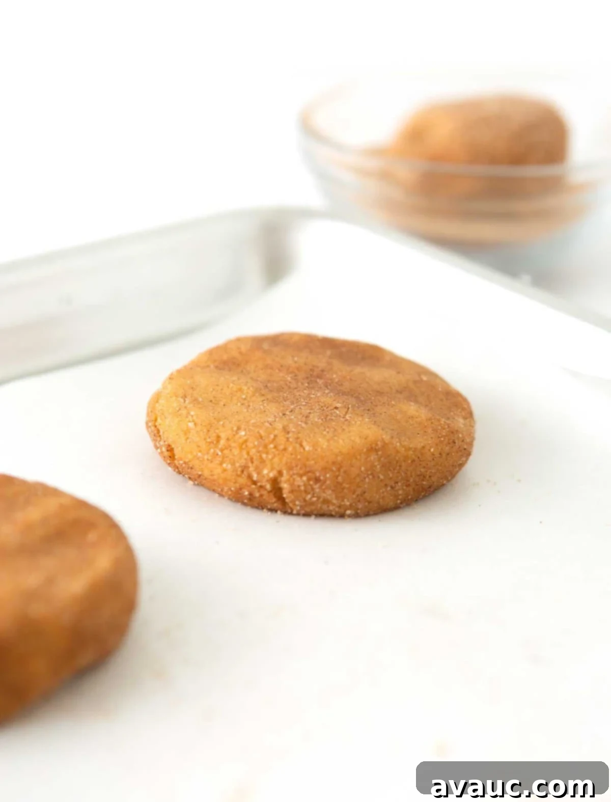 Flattening the top of a pumpkin snickerdoodle dough ball before baking to ensure even spreading.
