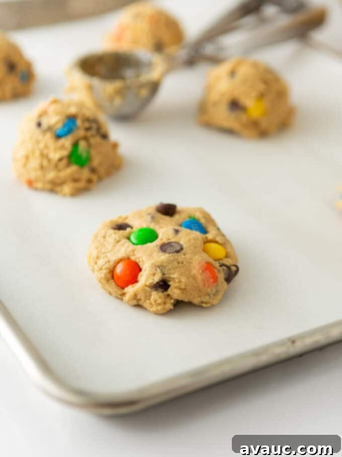 Flattened monster cookie dough balls with extra M&M's on top, arranged on a baking sheet, ready for the oven