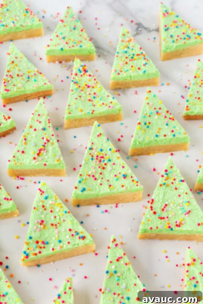 Festive Christmas Tree Sugar Cookie Bars 14 A festive arrangement of triangle Christmas trees made from 9x13 pan sugar cookie bars, adorned with green frosting and colorful sprinkles, ready for serving.