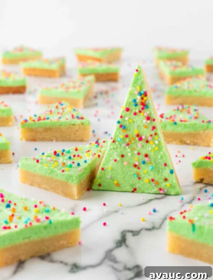Festive Christmas Tree Sugar Cookie Bars 3 Close-up of a hand holding a green Christmas tree sugar cookie bar, topped with vibrant nonpareil sprinkles, showcasing its soft texture and festive appeal.