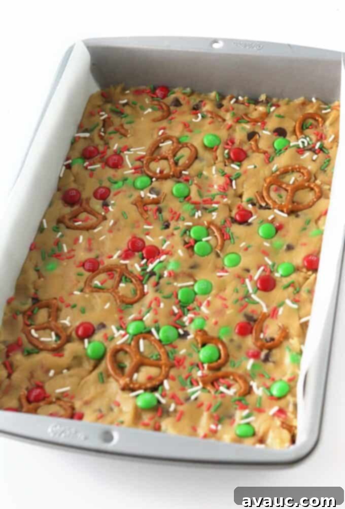 Festive Cookie Squares 8 Raw Christmas cookie bars dough pressed into a pan, topped with extra M&M's and sprinkles, ready for baking.