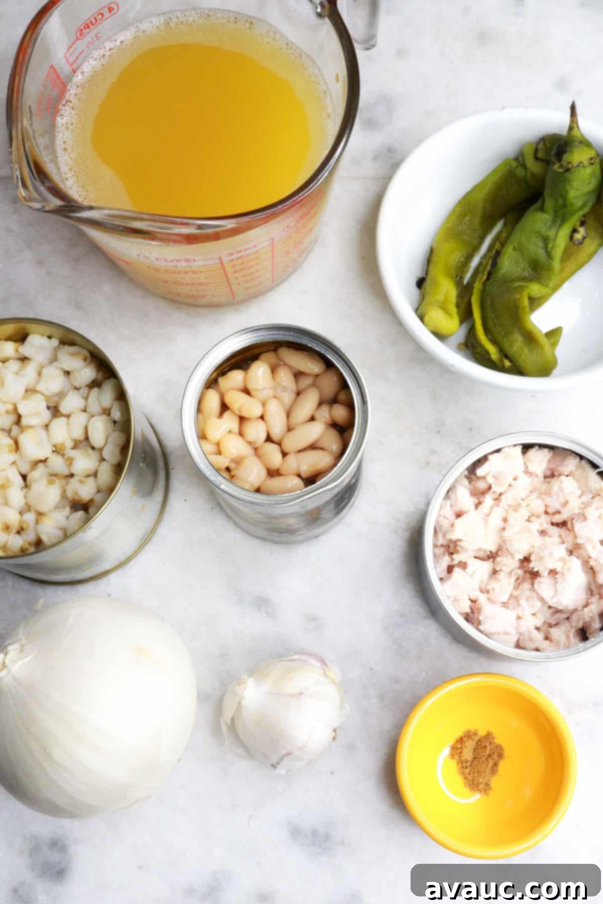 Foolproof White Chicken Chili with Hominy 3 Measuring cup with chicken broth, a bowl with roasted green chiles, a can of hominy, another with white beans and another with chicken, an onion, a head of garlic, a pinch bowl with cumin