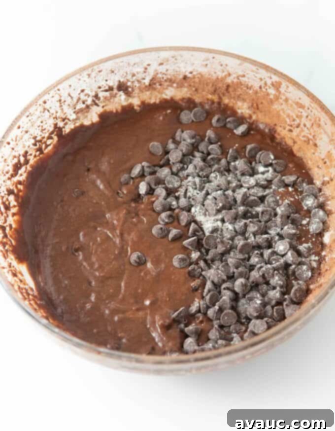 Glass bowl of chocolate banana bread batter with chocolate chips tossed in flour, ready to be folded in.